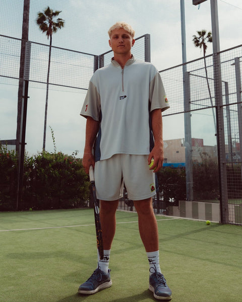 Person holding a tennis racket and ball on a tennis court with palm trees in the background